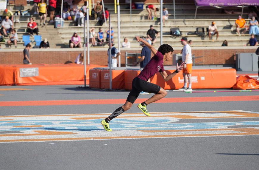 Athlete sprinting on track during a sunny outdoor sports meet.