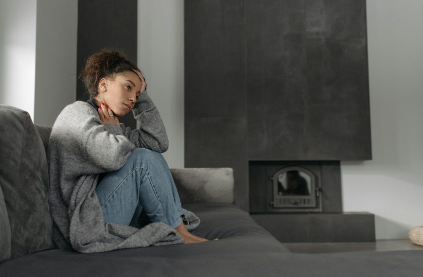 A woman in a cozy living room feeling unwell, sitting on a sofa with a thoughtful expression.